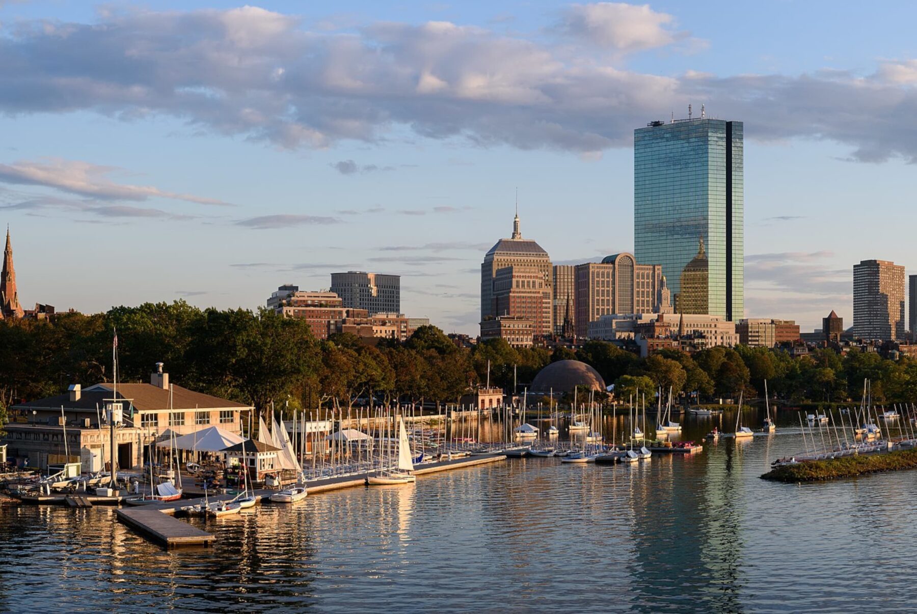 Bostoner Skyline bei Abendlicht mit Yachthafen im Vordergrund und dem spiegelnden John Hancock Tower im Wasser.