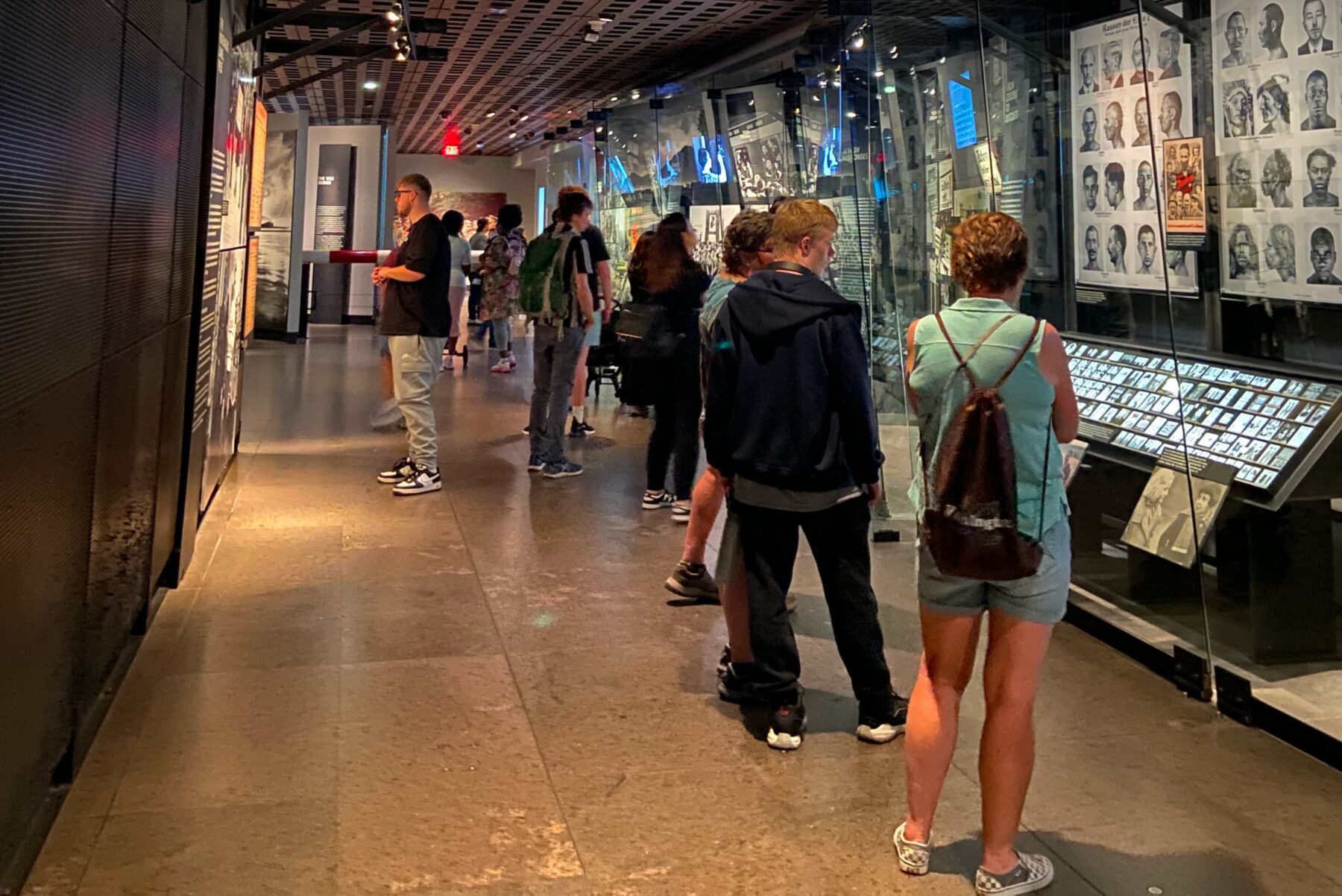 Menschen in Museumsgang blicken auf Glasvitrinen mit Fotos und Porträtwänden, einige stehen in einer Schlange.
