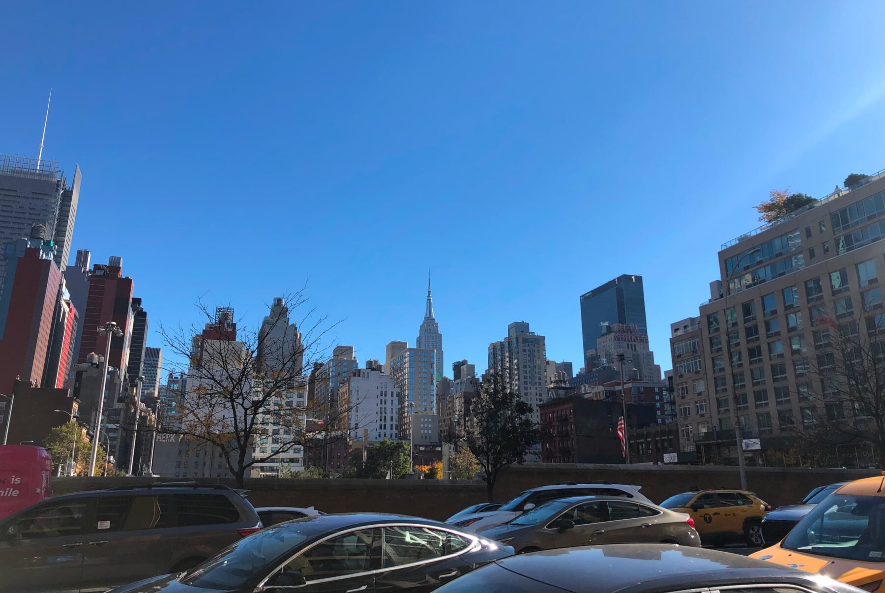 Parkplatz mit Autos und Taxis vor der Manhattan-Skyline, dem Empire State Building zentral vor klarem blauem Himmel