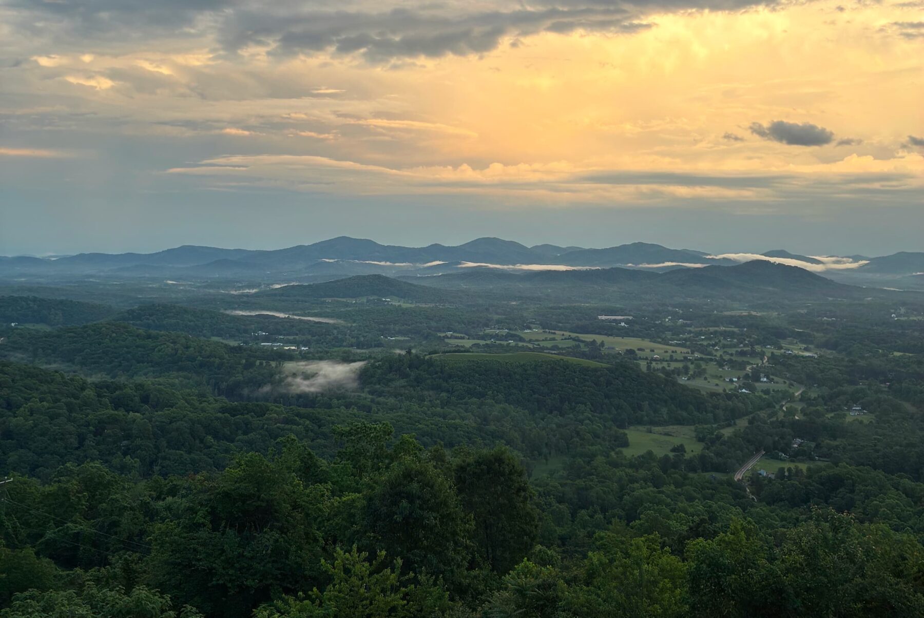 Shenandoah-Tal mit grünen Hügeln, Nebelschwaden im Tal und goldener Abendhimmel über fernen blauen Bergen.