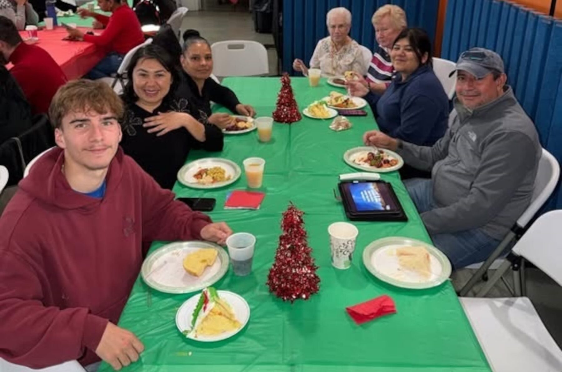 Schwestern von St. Joseph, Camden NJ, mit anderen an grün bedecktem Tisch, essen Kuchen; kleine rote Weihnachtsbäumchen.