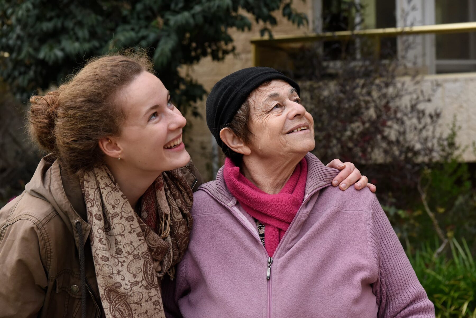 Clara Geberth und Ruth Levi: junge Frau umarmt ältere, beide lächeln und schauen nach oben; ältere mit Mütze und rosa Schal