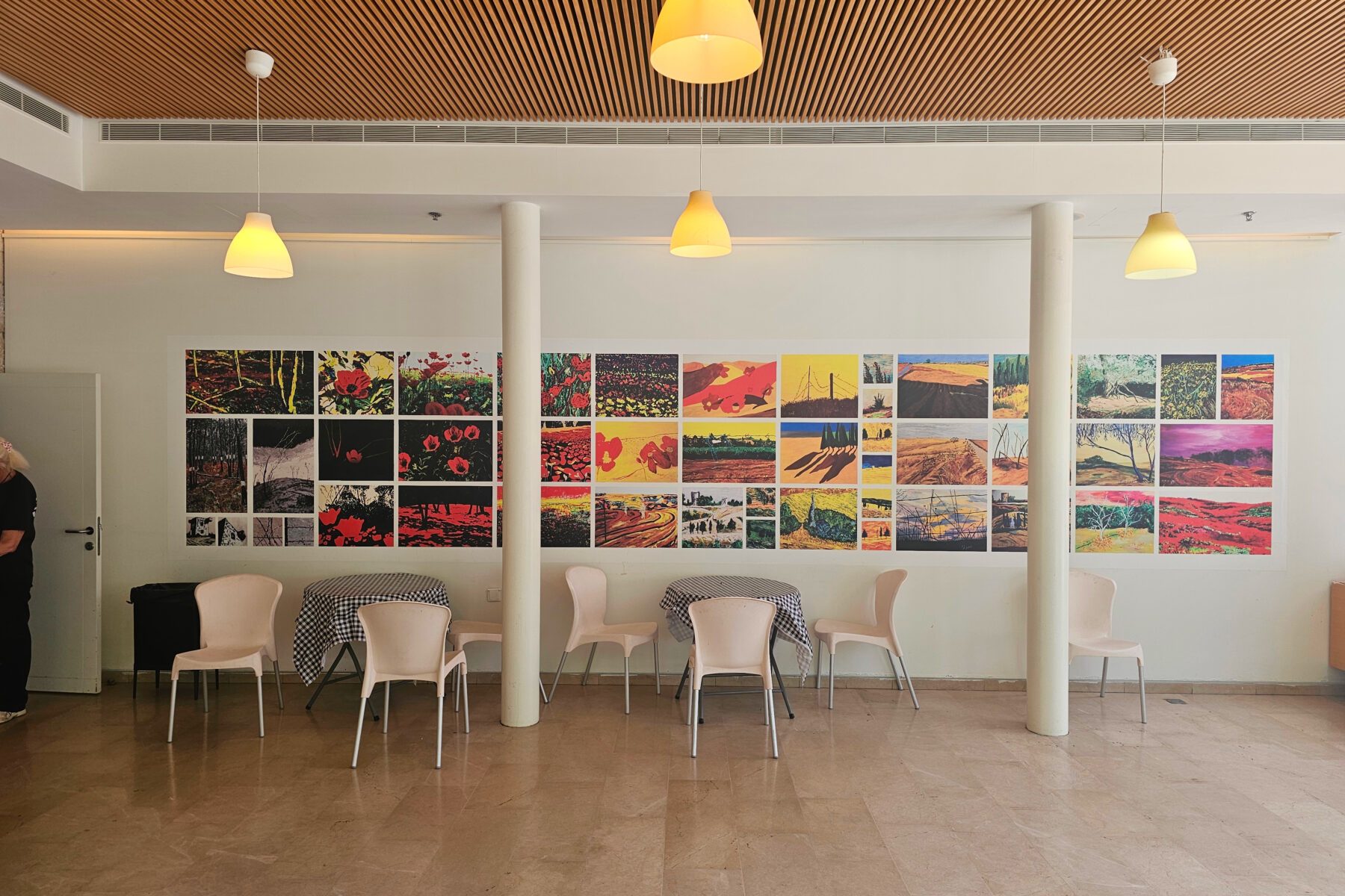 Foyer von Yad‑Ben‑Zvi, Jerusalem: lange Wand mit bunten Quadraten, drei Tische mit karierten Decken, helle Stühle und Lampen