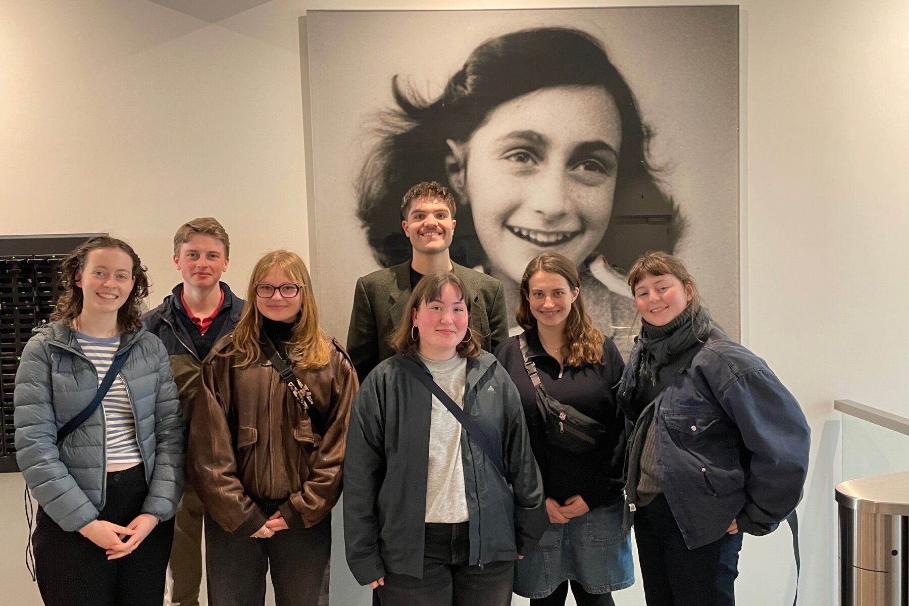 ASF-Freiwillige posieren vor großem Schwarzweißporträt an der Wand im Anne-Frank-Haus, Innenraum.