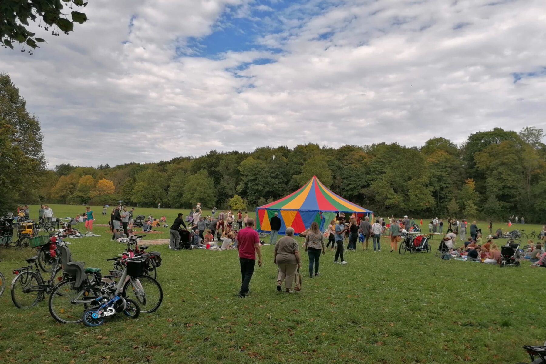 Buntes Festzelt beim Grandhotel-Festival Augsburg, Menschen auf Picknickdecken, Fahrräder im Vordergrund, Bäume dahinter