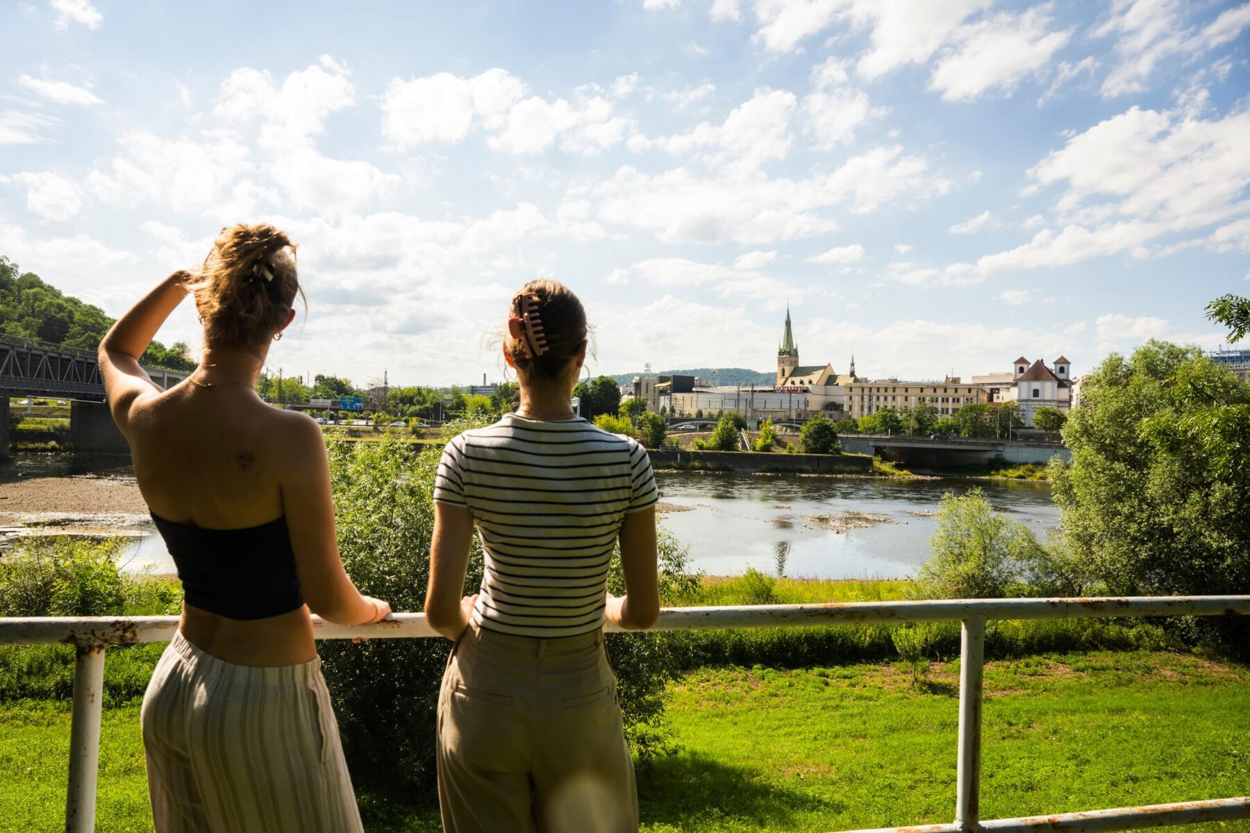 Zwei junge Frauen lehnen am Geländer und blicken über die Elbe auf Ústí nad Labem mit Kirche und Brücke.