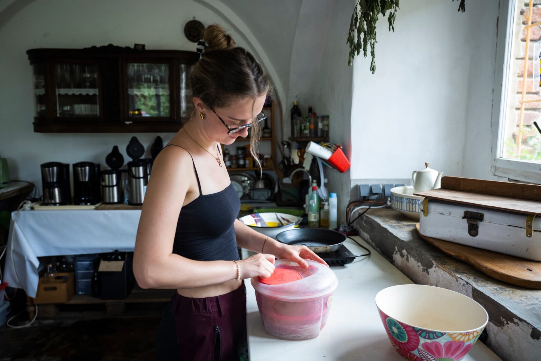 Freiwillige in schwarzem Top und Brille verschließt roten Plastikbehälter auf weißer Küchenarbeitsplatte