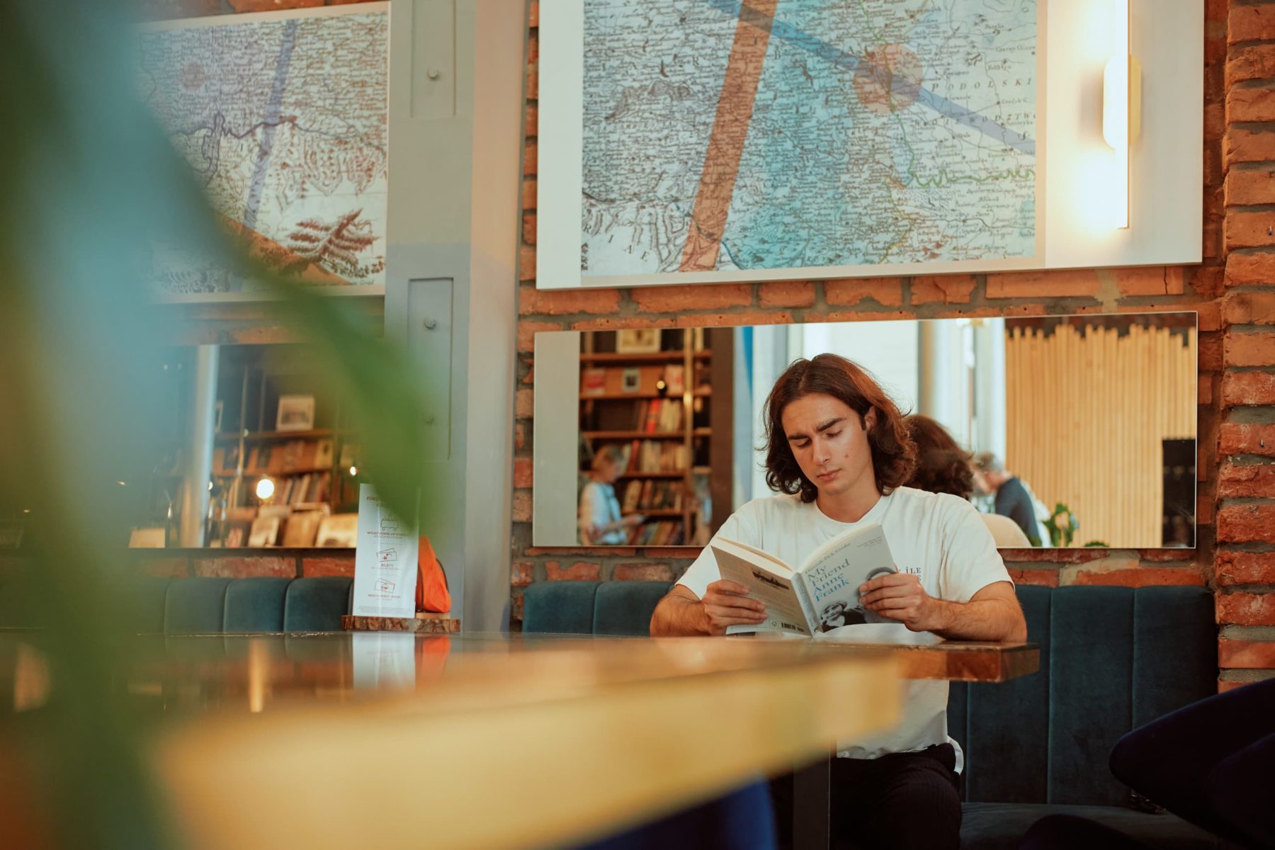 Ein Mann liest ein Buch in einem Café. Im Hintergrund sind Bücherregale und eine Karte an der Wand.