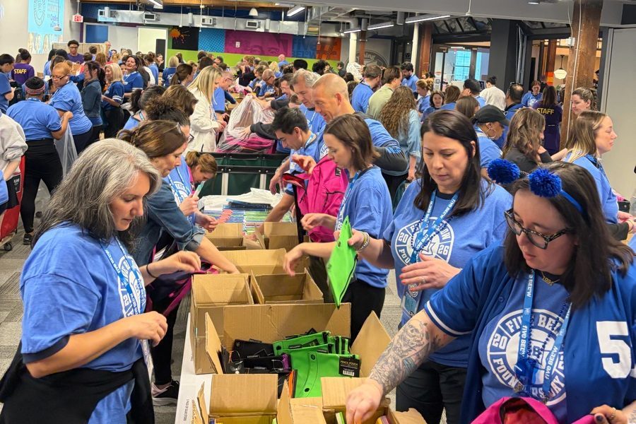 ASF-Freiwillige in blauen Shirts packen bei Cradles to Crayons Philadelphia an Tischen Schultaschen und Schulmaterial.
