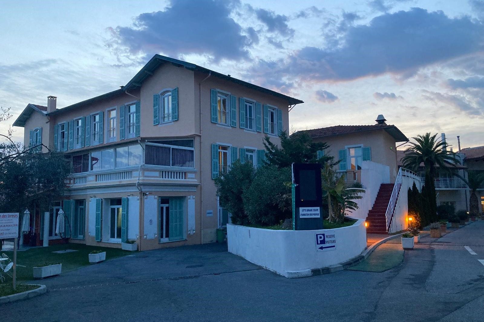 ASF-Haus La Colline in Nizza bei Dämmerung, helles Gebäude mit grünen Fensterläden, Veranda und Außentreppe.