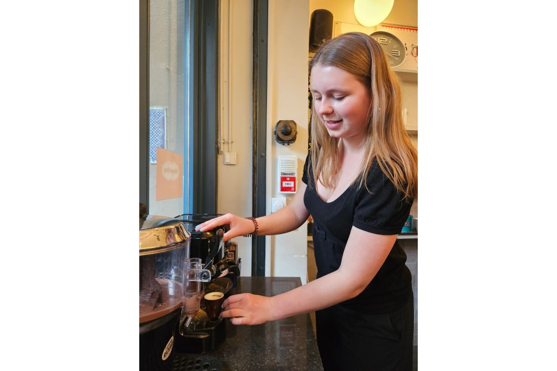 Junge Barista im Café des Psaumes (Paris) betätigt Espressomaschine, füllt kleine Tasse und lächelt.