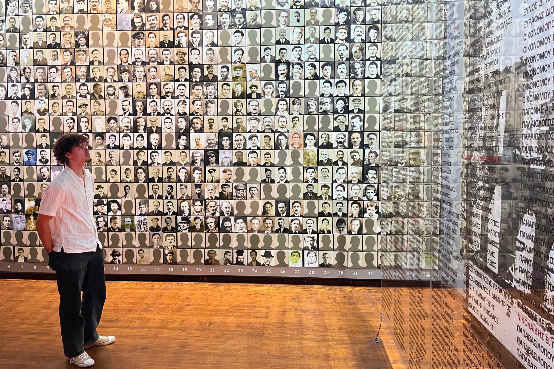 Besucher vor Wand mit hunderten Porträtfotos und Glasplatten mit griechischen Namen im Holocaustmuseum Kalavryta