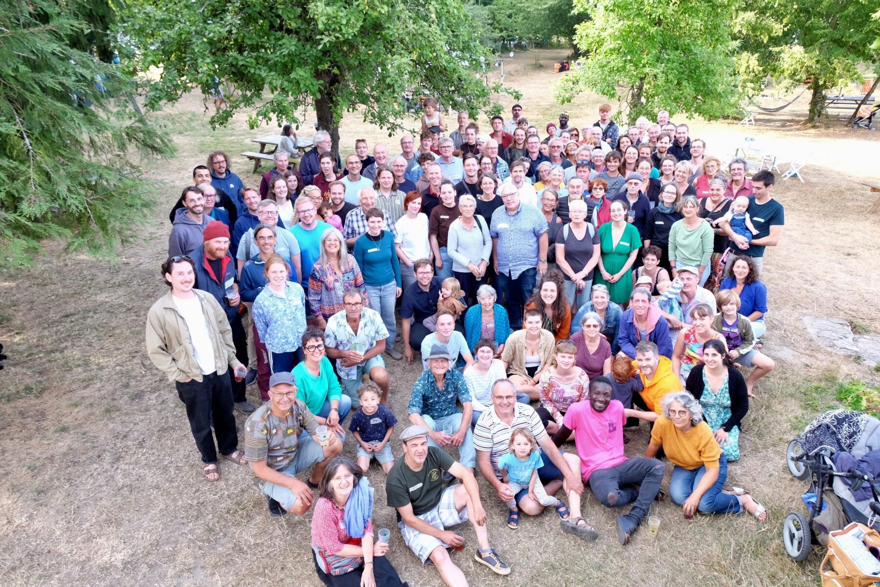 Große Gruppe posiert lächelnd auf trockener Wiese unter Bäumen beim ASF-Jubiläum in St. Jean, Frankreich.