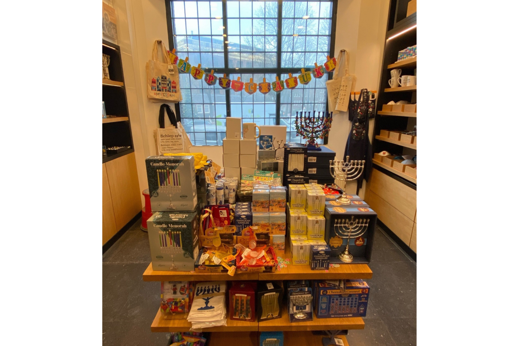 Laden-Display im Jüdischen Museum Amsterdam: Regal mit Chanukka-Kerzen, Menorot, Dreideln und 'Happy Chanukah'-Girlande