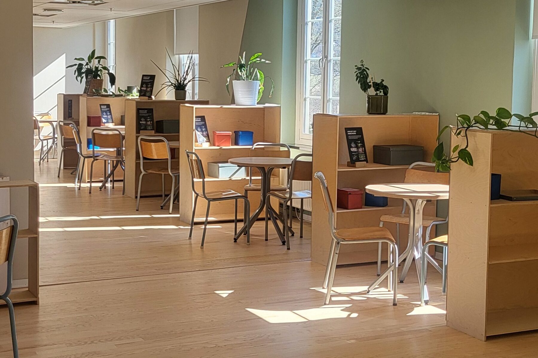 Heller Lernraum im ASF Falstad-Zentrum: Holztische und Stühle an Trennregalen, Fensterlicht und grüne Pflanzen.