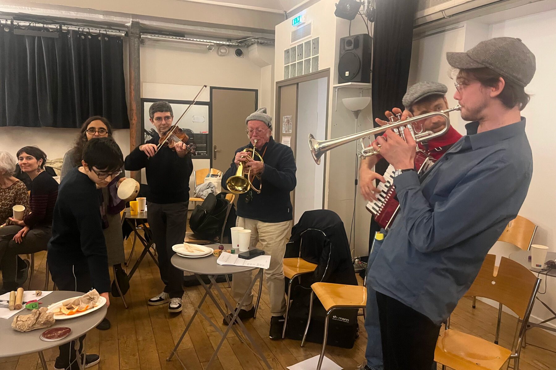 Musiker mit Trompete, Violine und Akkordeon bei Chanukka‑Feier in Paris 2026, kleine Gruppe in schlichtem Saal