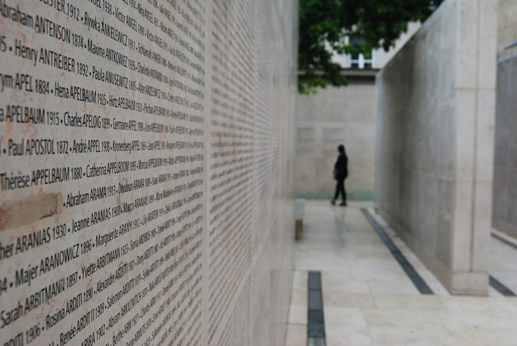 Gedenkstätte Shoah Paris: Namenstafel an Mauer vorn, langer Gang und eine einzelne, unscharfe Person hinten.