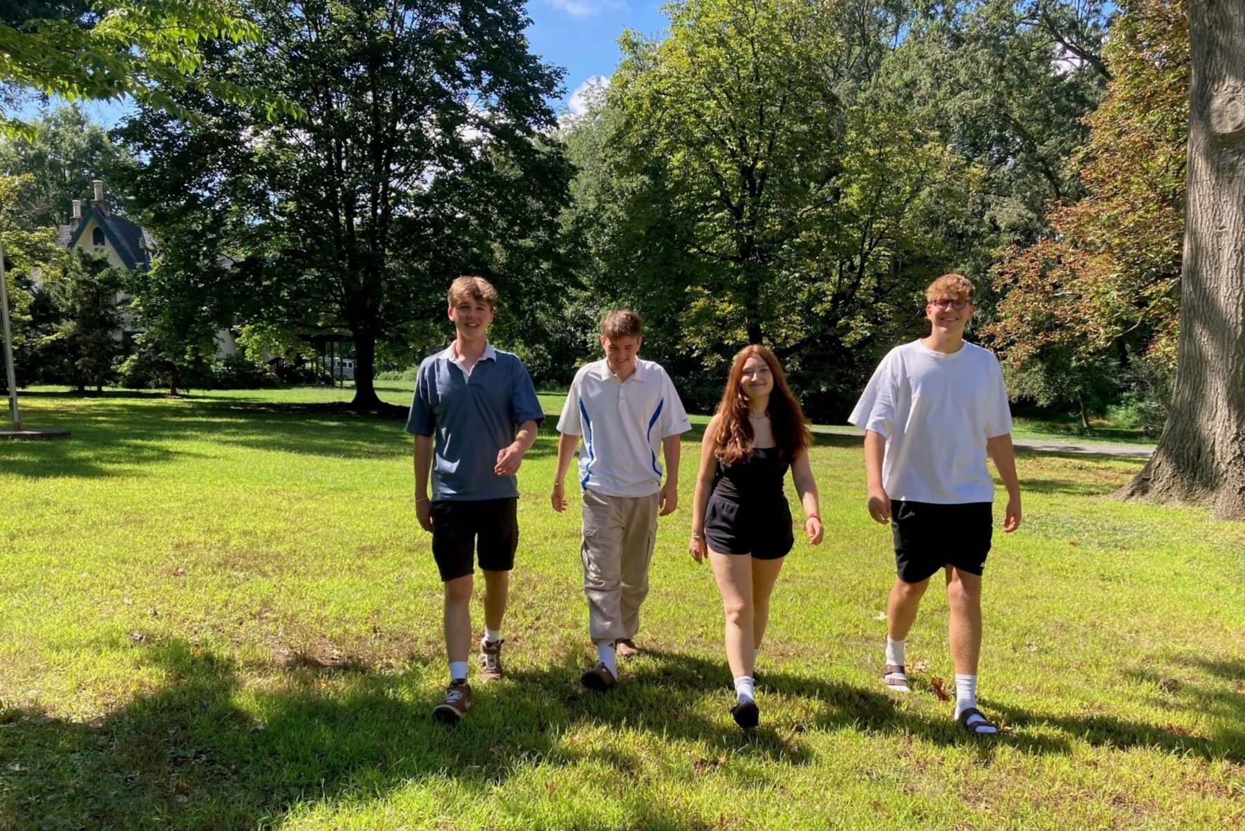 Vier Jugendliche beim ASF‑Orientierungstag in Philadelphia, spazierend über sonnenbeschienene Parkwiese vor Bäumen.