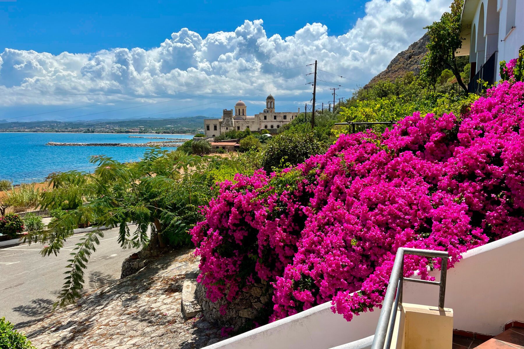 Leuchtende pinke Bougainvillea an Balkon, Blick auf das Meer und die Orthodoxe Akademie Kreta unter blauem Himmel.