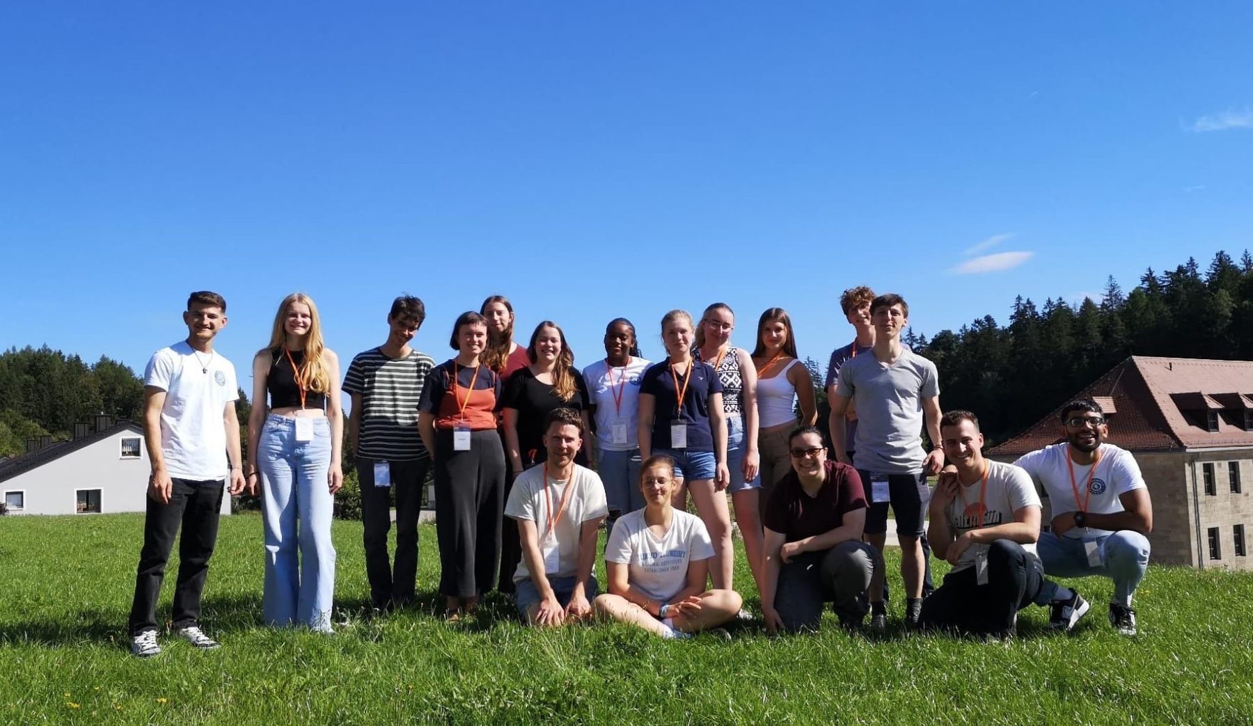 Gruppe junger Menschen beim ASF-Sommerlager 2023 in Flossenbürg auf einer Wiese, blauer Himmel, Gebäude im Hintergrund.