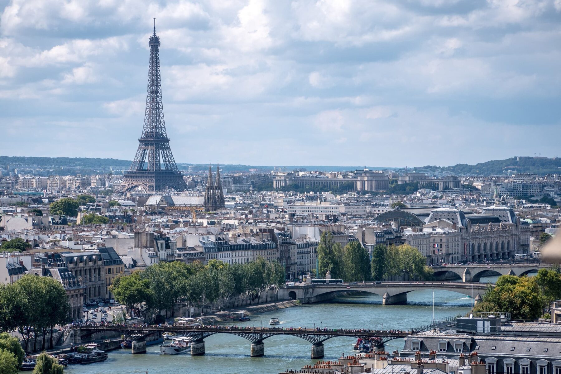 Eiffelturm über Pariser Dächer, Seine mit mehreren Brücken und Booten, bewölkter Himmel