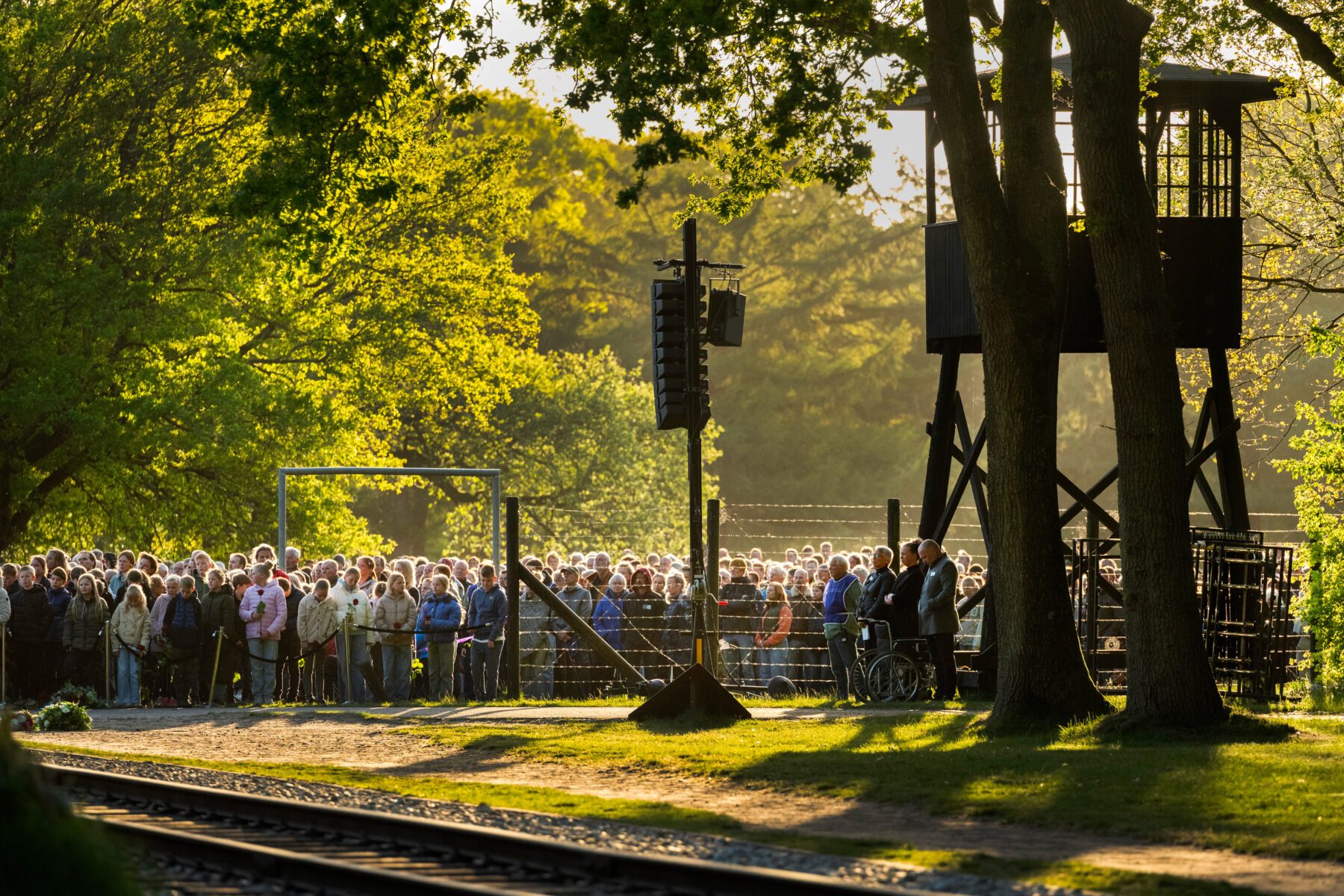 Menschenmenge bei Gedenkveranstaltung in der Gedenkstätte Kamp Westerbork, Abendlicht, Wachturm und Bahngleise vorn