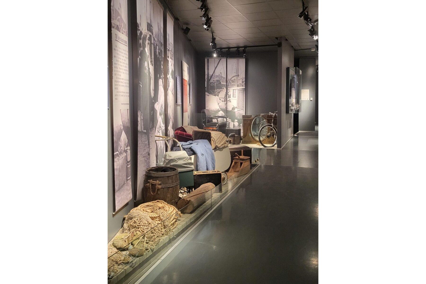 Wiederaufbaumuseum Hammerfest: Ausstellung mit Fischernetz, Fass, Fahrrad und Möbeln vor schwarz-weißen Fototafeln.
