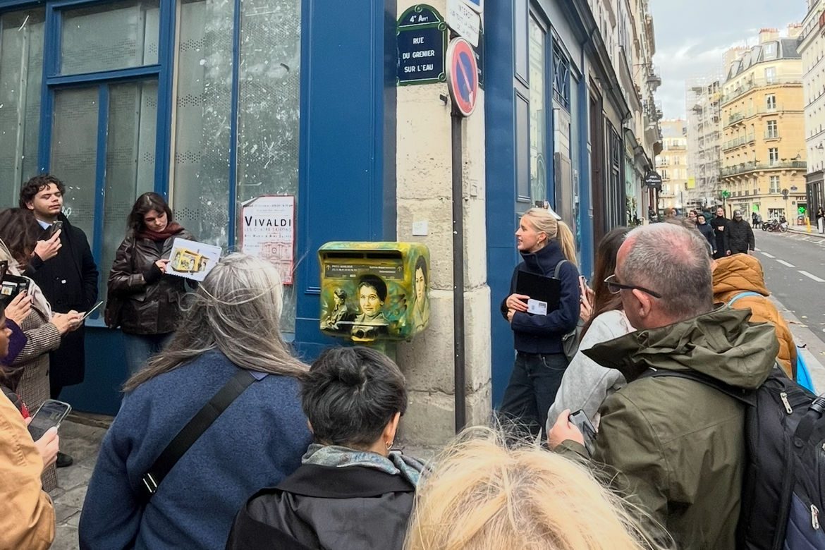 Teilnehmer einer ASF/Yahad-in-Unum-Führung in Paris um einen bemalten grünen Briefkasten an blauer Hauswand.