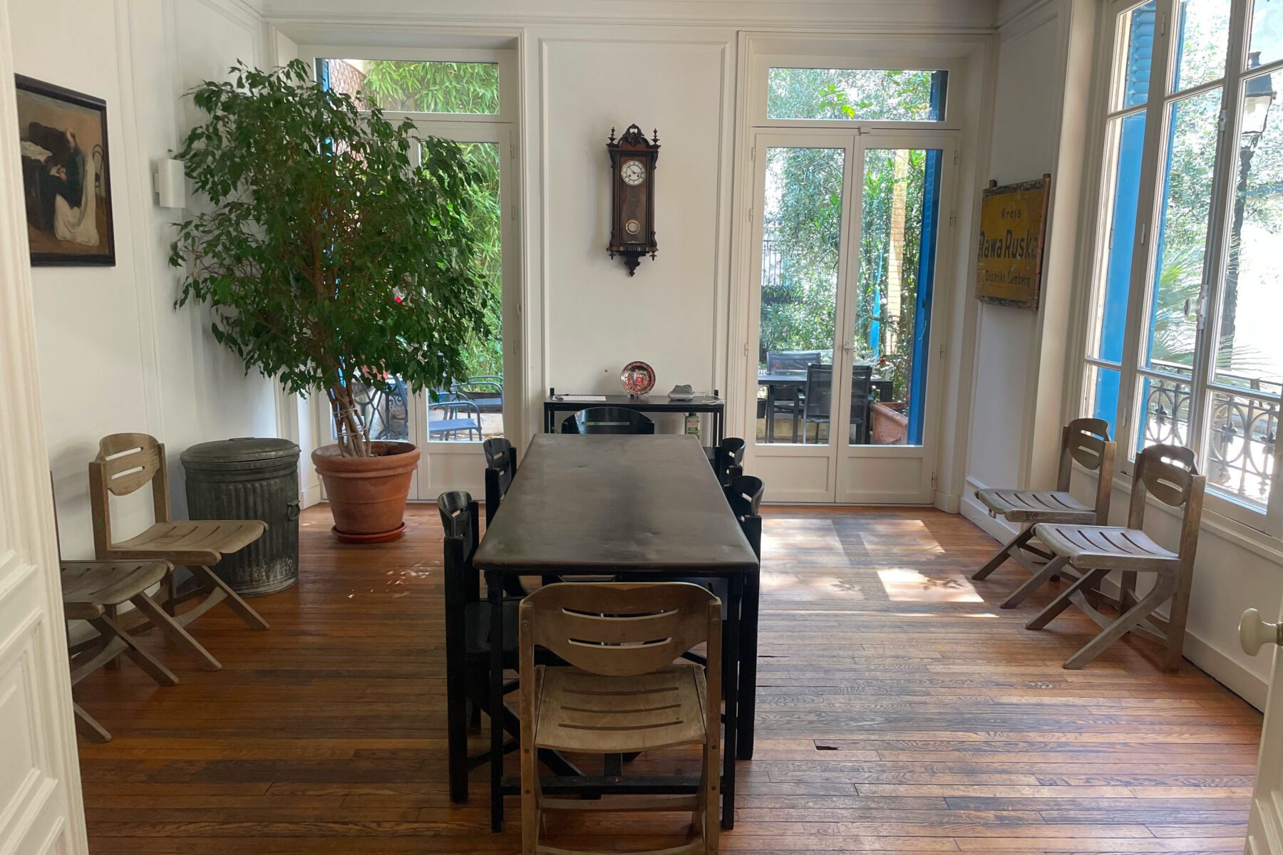 Salon bei ASF 'Yahad in Unum', Paris: langer Tisch mit Klappstühlen, Topfpflanze, Wanduhr und Glastüren zum Garten.