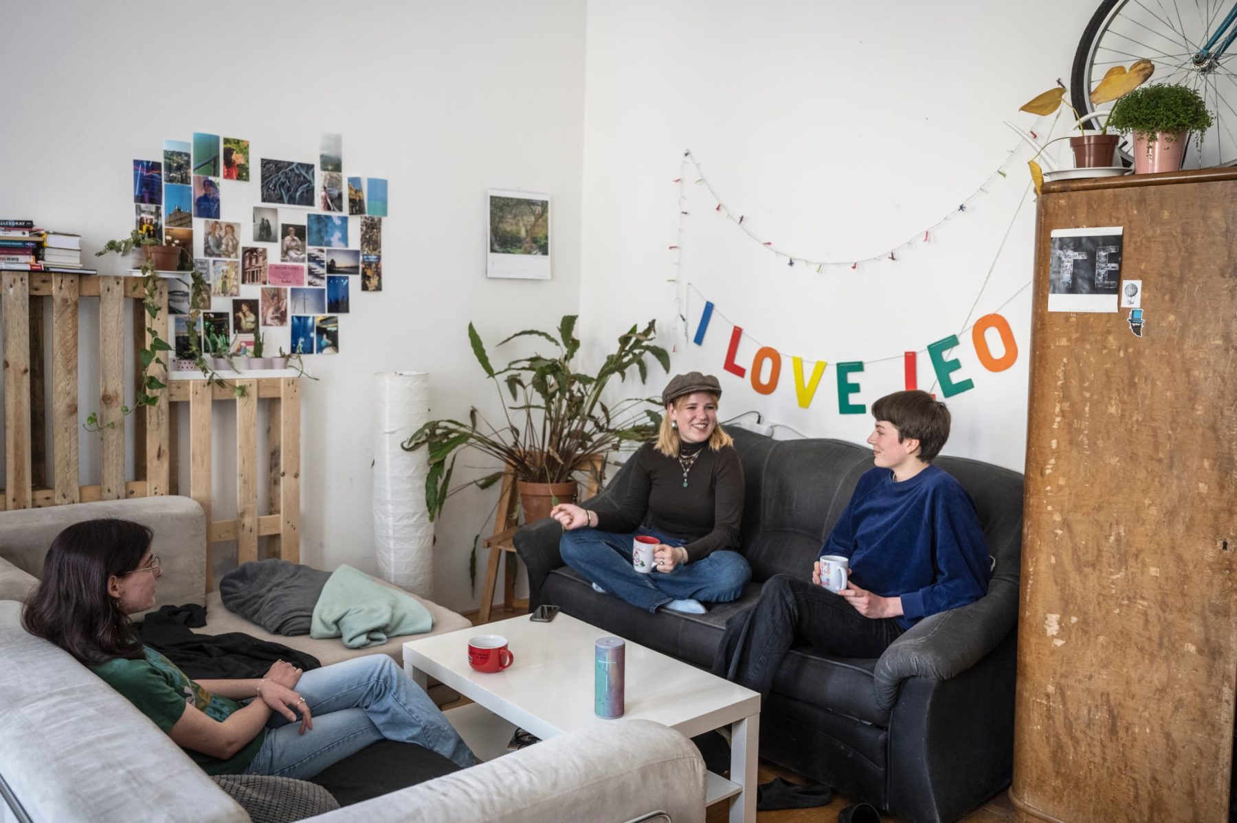 Drei Personen sitzen lachend auf Sofas in einem gemütlichen Zimmer in Brno mit buntem I LOVE LEO Banner.