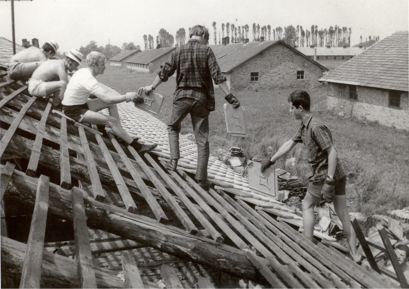Добровольцы из ГДР ремонтируют крышу в Польше, 1965 год. На заднем плане видны кирпичные здания и деревья.
