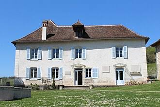 Maison d'Izieu: grande maison blanche à deux étages, volets bleus, toit en tuiles, pelouse verte sous ciel bleu.